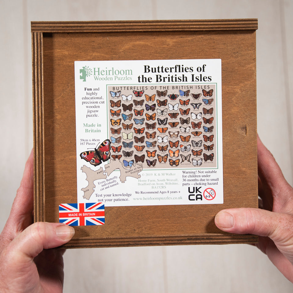 A dark wooden box with a sticker stuck on top with the details of the Heirloom Puzzles butterfly puzzle. The box is being held at the bottom