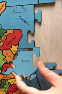A partially made puzzle of the counties of the British isles. A hand is holding the sea area piece labelled Forth.