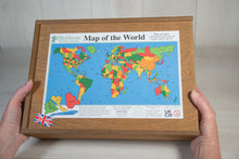 Load image into Gallery viewer, Two hands hold a large wooden box that contains a wooden jigsaw of the countries of the world