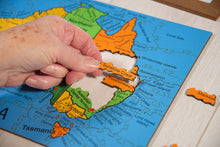 Load image into Gallery viewer, Hand placing a puzzle piece on a map of Australia with colored regions.