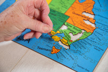 Load image into Gallery viewer, Hand placing a puzzle piece on a map of Australia with colored regions.