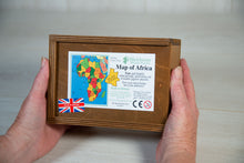 Load image into Gallery viewer, Two hands hold a warm brown wooden box, with a sticker stuck to the lid showing the details of the Map of Africa jigsaw puzzle it contains