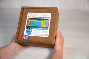 Two hands hold a wooden box contain a wooden jigsaw puzzle of the periodic table