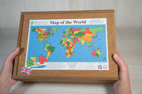 Two hands hold a large wooden box that contains a wooden jigsaw of the countries of the world